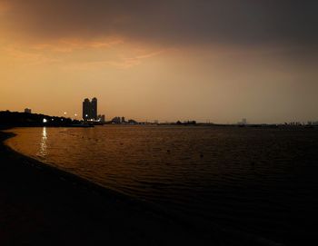 Silhouette buildings by sea against sky during sunset
