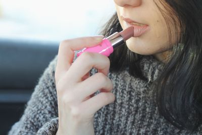 Midsection of woman applying lipstick 