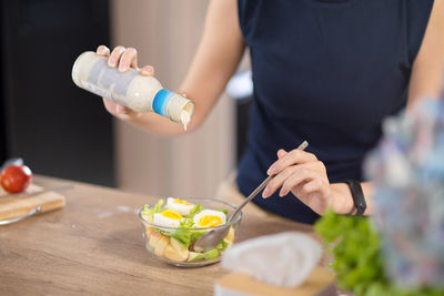 Midsection of woman holding bottle on table