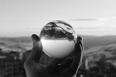 Close-up of hand holding crystal ball against sky during sunset