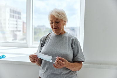 Smiling senior woman holding mask against window