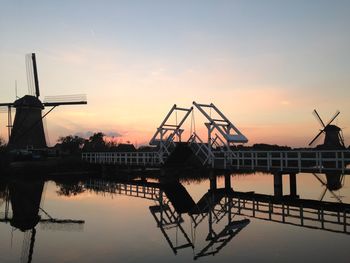 Silhouette cranes by lake against sky during sunset
