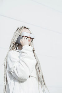 Low angle view of woman with dreadlocks talking over smart phone while standing against wall