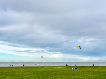 People on grassy field by sea against cloudy sky