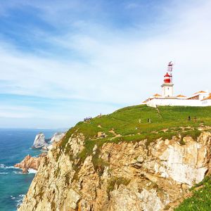 Lighthouse on cliff by sea against sky