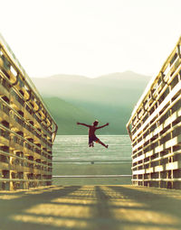 Rear view of boy jumping at beach against clear sky