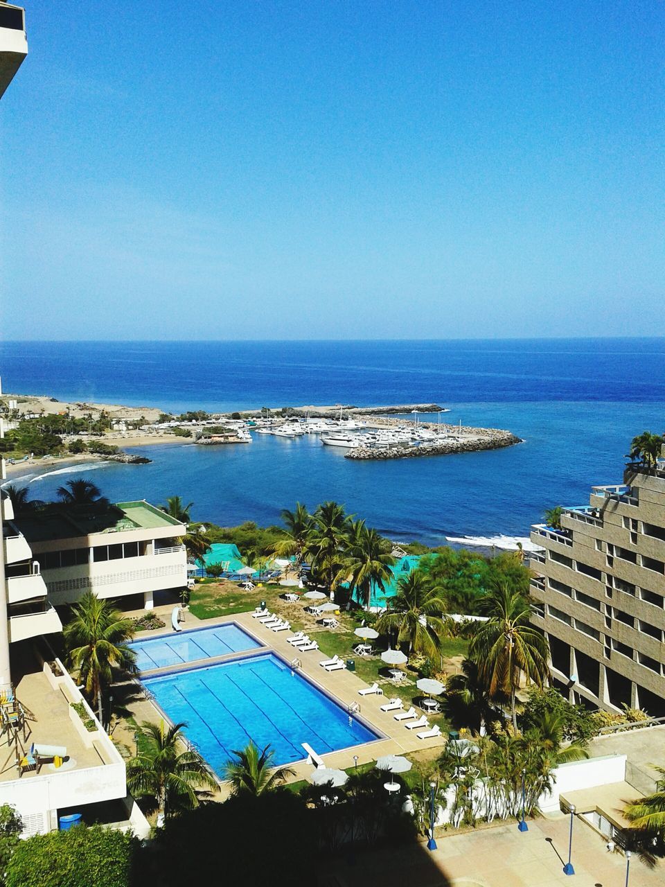 sea, horizon over water, water, clear sky, blue, building exterior, built structure, architecture, copy space, high angle view, tree, scenics, beach, nature, sky, nautical vessel, palm tree, beauty in nature, tranquil scene, day