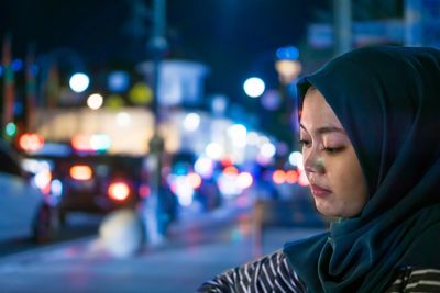 Close-up of young woman standing on illuminated street at night