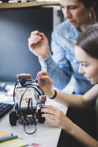 Female teacher assisting teenage student preparing robot on desk in classroom at high school