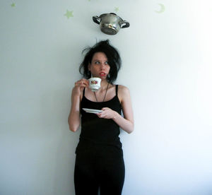 Cooking pan over woman holding cup and saucer against wall at home