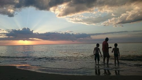 Father and sons standing in sea against sky during sunset