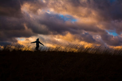 Silhouette person on field against sky during sunset