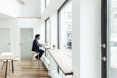 Mature businessman working on laptop while sitting by window in office