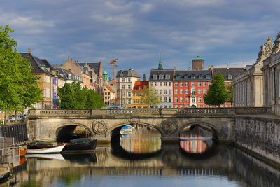 Bridge over river by buildings in city against sky