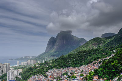 Cityscape by mountain against cloudy sky