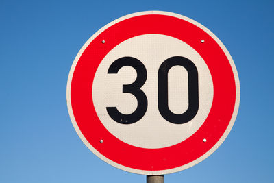 Low angle view of road sign against clear blue sky