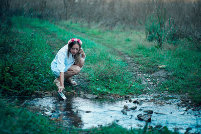 Full length of young woman filling water from stream in container at forest