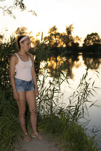 Woman standing by plants against lake during sunset