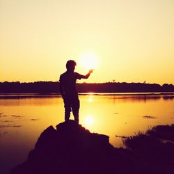 Silhouette of person by lake at sunset