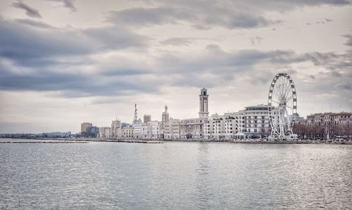 View of buildings by river against cloudy sky