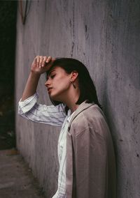 Young woman looking away while standing against wall