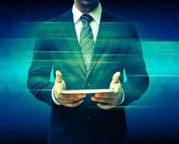 Digital composite image of businessman holding digital tablet against colored background