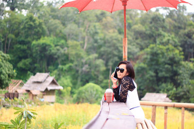 Young woman talking on mobile phone while sitting against trees