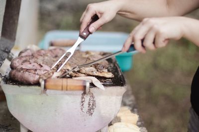 Cropped hands cooking meat on barbecue