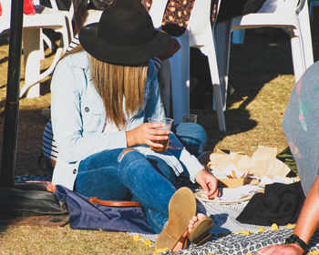 Woman holding beer glass while sitting on field