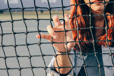 Midsection of woman holding chainlink fence in playground