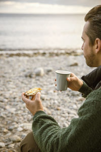 Cropped image of man eating snack with coffee at beach