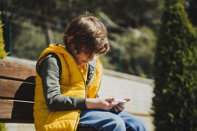 Boy using smart phone sitting on bench