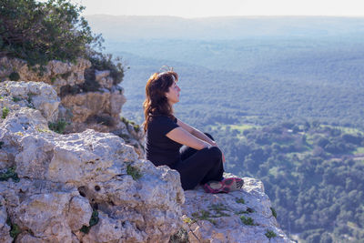 Side view of woman relaxing on rocky cliff