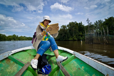 Full length of woman using mobile phone while sitting on rowboat