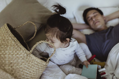 Male toddler peeking in basket while father sleeping on bed at home