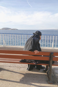 Man sitting on bench by sea against sky