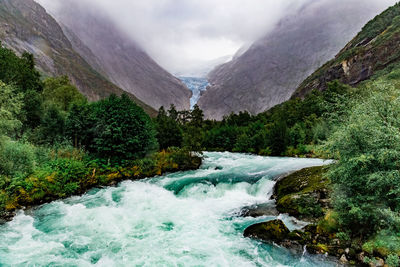 Scenic view on briksdal glacier, river and norwegian mountains against cloudy dramatic sky