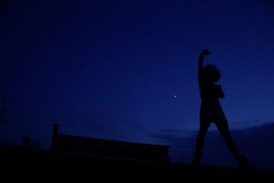 Low angle view of silhouette woman standing against blue sky