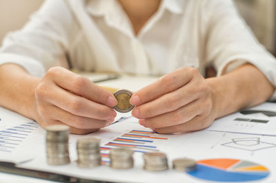 Midsection of businesswoman holding coin at desk in office