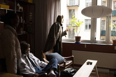 Woman looking through window on vacation with friends in apartment