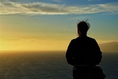 Rear view of silhouette woman looking at sea against sky during sunset