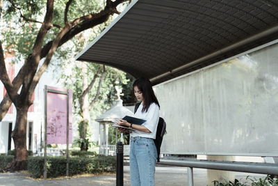 Woman holding mobile phone while standing on tree