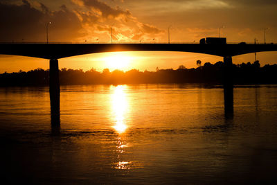 Silhouette bridge over river against sky during sunset