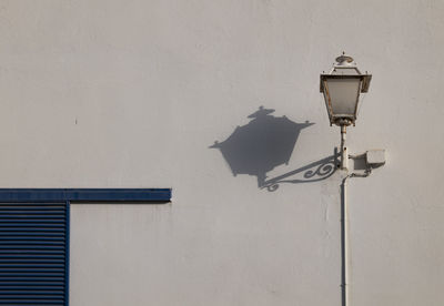 Low angle view of street lamp and shadow with blue window on white wall