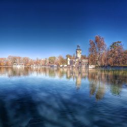 Scenic view of lake by buildings against clear blue sky