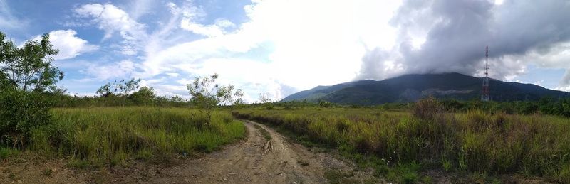 Dirt road amidst field against sky