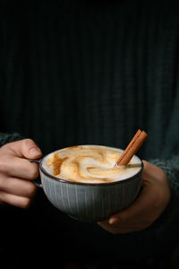 Woman holding cup of cappuccino with cinnamon sticks