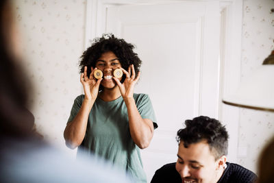 Portrait of smiling young woman holding cookies while enjoying with friend at home