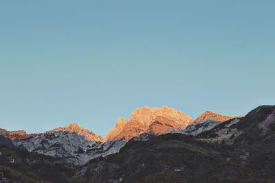 Low angle view of snowcapped mountains against clear blue sky