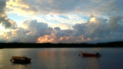 Boats in calm lake against cloudy sky